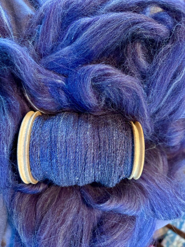 A bobbin of purple shetland wool singles resting on the remaining unspun fiber