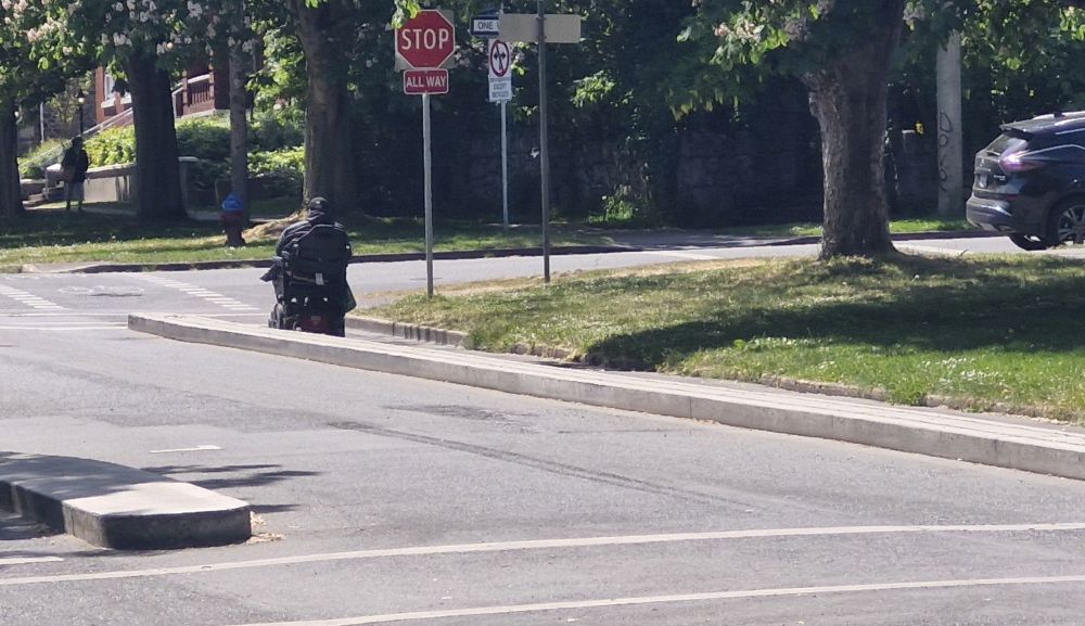Person on wheelchair traveling in a one-way protected bike and roll lane.