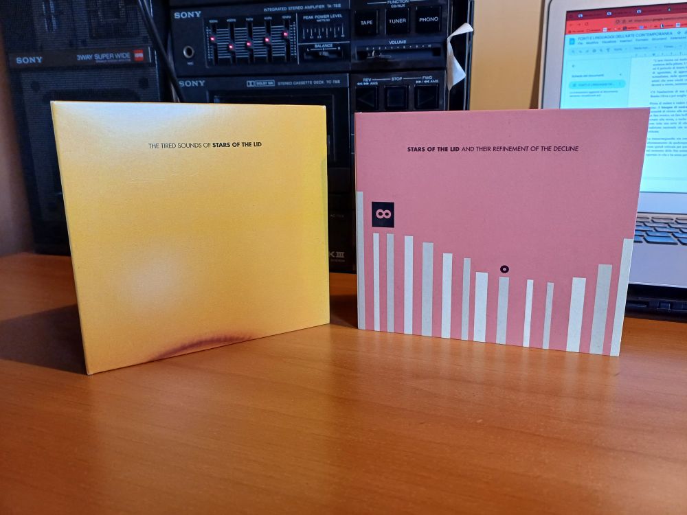 Due cd messi in verticale sopra una scrivania. Sullo sfondo uno stereo e un pc aperto.

I cd sono "The Tired Sounds of Stars of the Lid" e "Stars of the Lid and Their Refinement of the Decline"