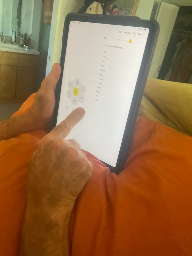 Husband’s hands holding his iPad in bed displaying the NYT Spelling Bee game. 