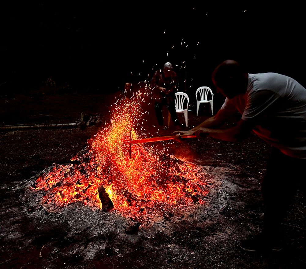 A red glowing burn pile being poked releasing a burst of sparks into the darkness. 
