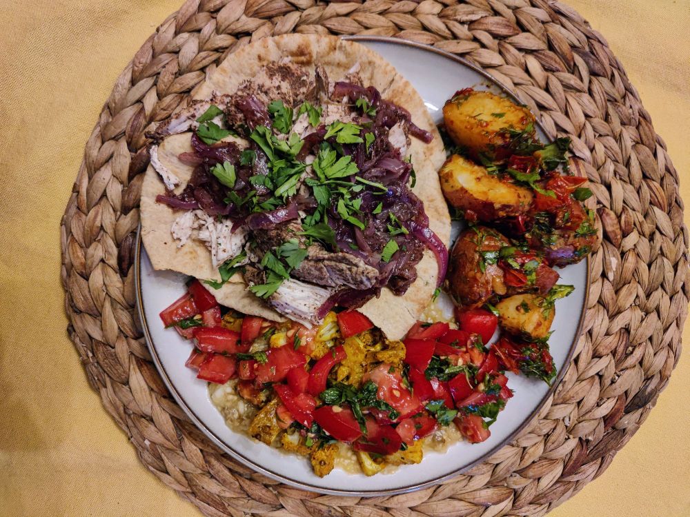 picture of roasted chicken and red onions on flax pita with like a boatload of sumac, roasted baby potatoes and fried garlic and tomatoes, and burnt eggplant with roasted cauliflower and salsa