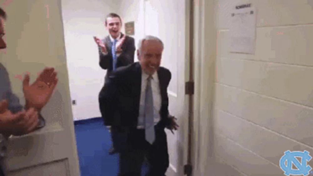 a man in a suit and tie is walking through a doorway while two other men applaud behind him