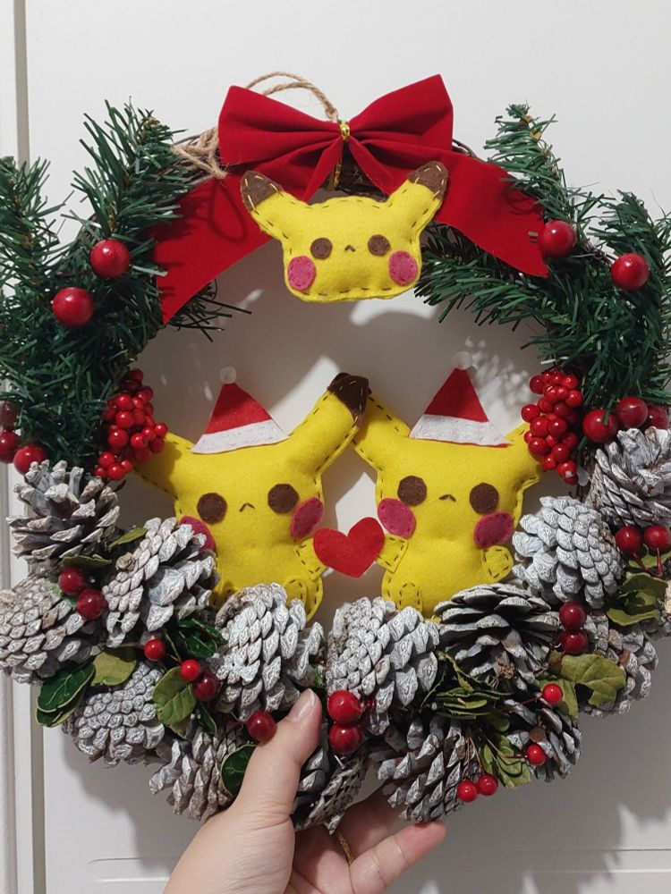 Guirlanda com casal de Pikachus natalinos e um laço com enfeite de Pikachu, os Pikachu são feitos de feltro