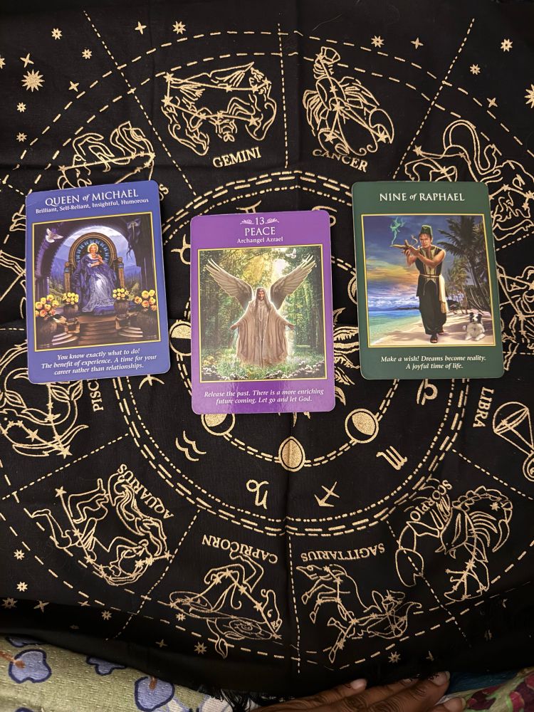 Three tarot cards on a piece of fabric. Queen of Michael, Peace and Nine of Cups.