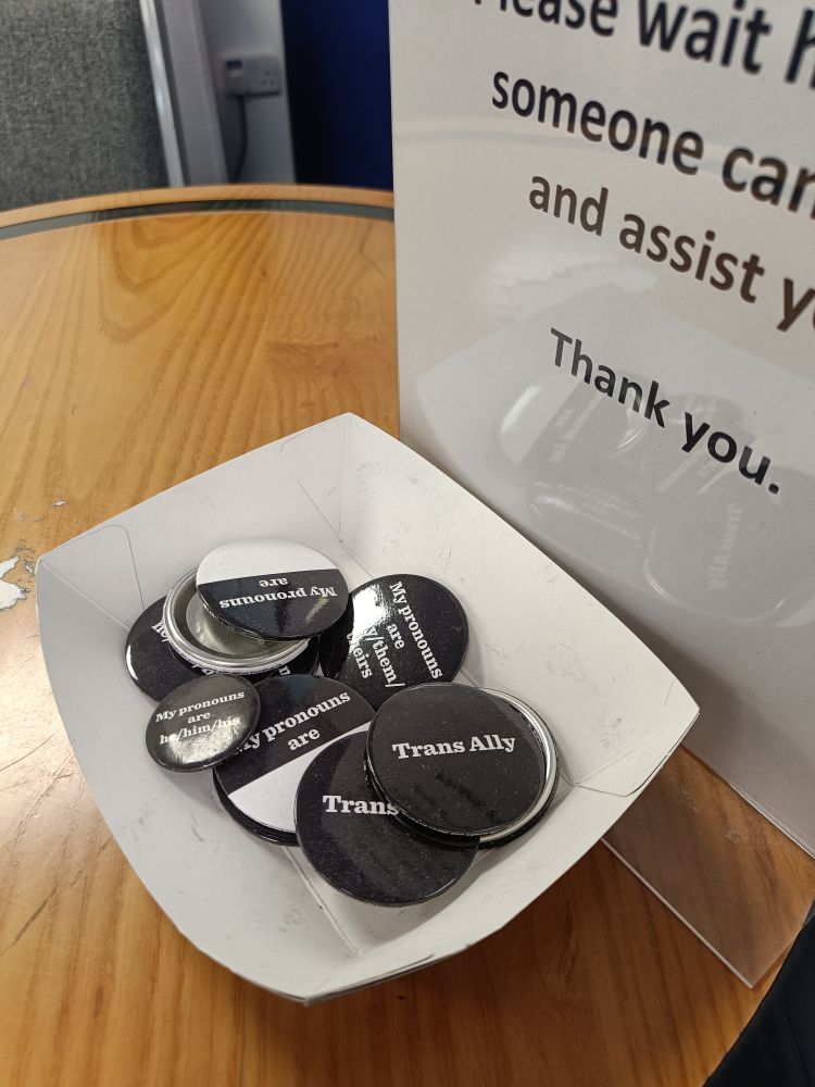 A pile of badges in the HR office saying things like "trans ally" and "my pronouns are..."