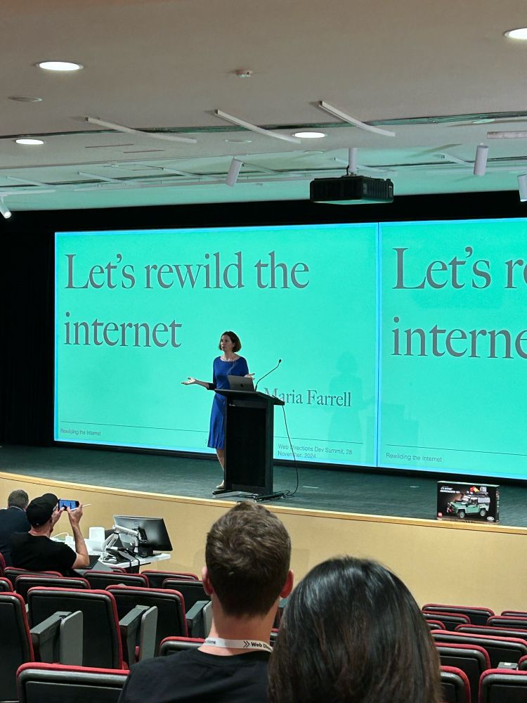 Maria on stage in front of an audience. The screen behind her says Let’s Rewild The Internet