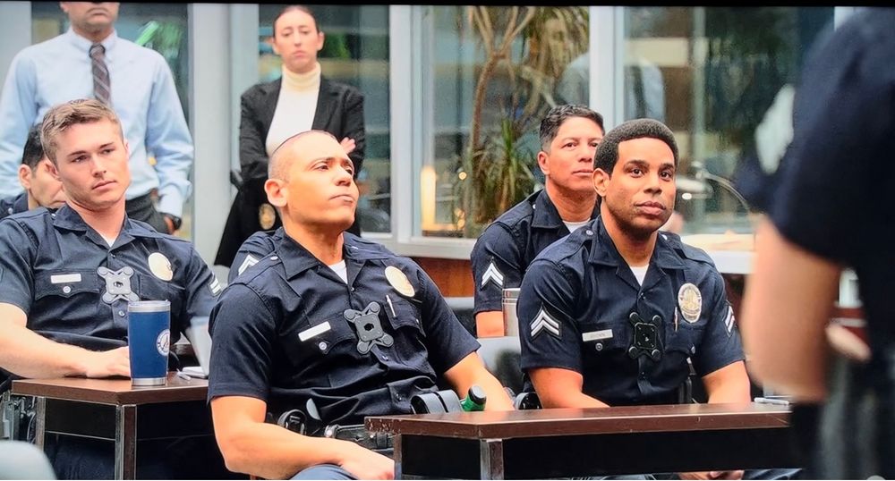 a screen grab from a scene in this season’s finale of The Rookie where I am standing behind a bunch of cops as a detective doing a good job looking unimpressed 