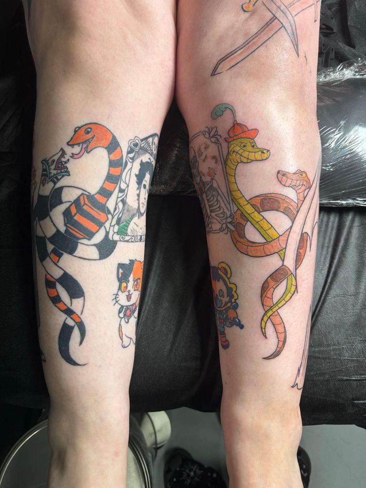 Photo of both legs showing Kaa and Sir Hiss on one shin and the Beetlejuice sandworm and gift-eating snake from The Nightmare Before Christmas on the other. 
