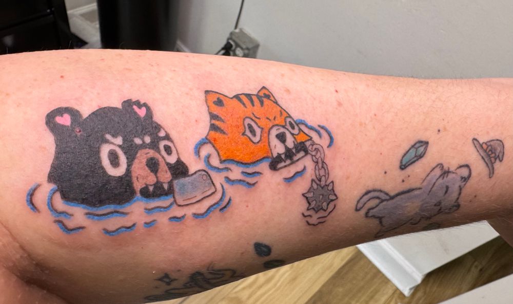 Photo of my left forearm featuring a tattoo of a bear and tiger coming up out of water. The bear has a butcher knife in her teeth and the tiger a mace. 