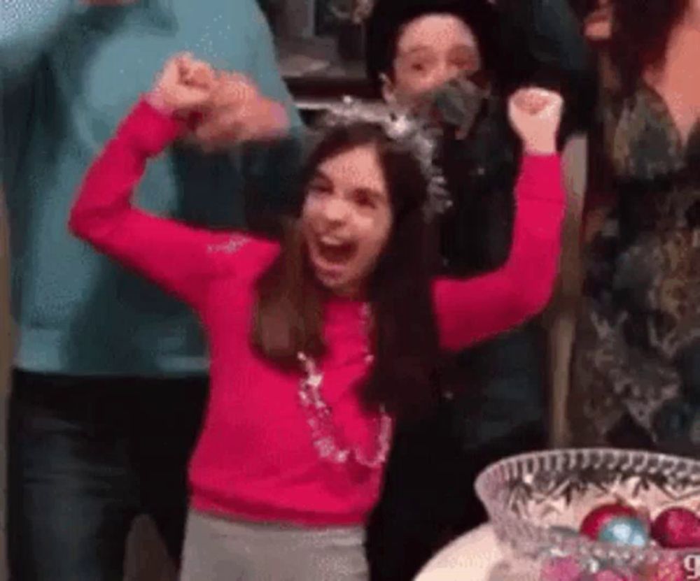 a girl in a pink sweater is raising her arms in the air while standing in front of a group of people .