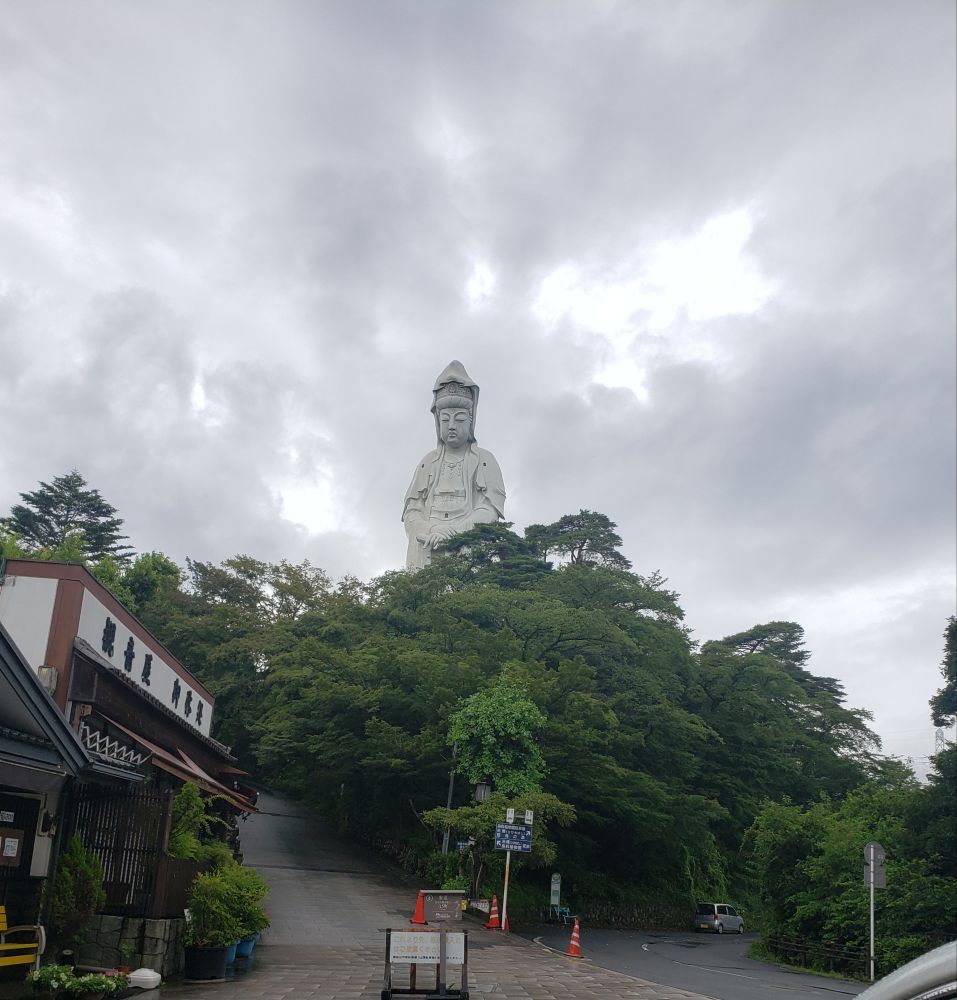 A rainy day photo of the Takasaki Kannon looming over the trees next to a small shrine 