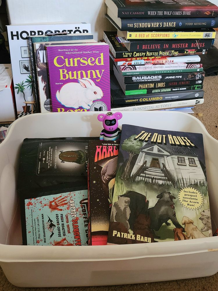 Hoo-boy, this is a lot to describe. While Webberly calls this chaotic mess his "To Read pile," it's really just an assortment of heaps, stacks, and slouching pillars of books, vaguely arranged by theme, author, or impulse. Growlix the Lookah Bear stares in a judgmental fashion at the books that somehow ended up sorted into a basin with the horror coffees. Jeezum-Crow, please don't make me type in all these authors and titles. Should anyone ever read these words and have a legit need for me to specify what's in the photo, fine, just... when you demand, be kind, eh? 