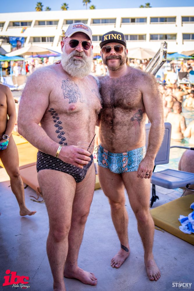two handsome men stand side by side at a pool party