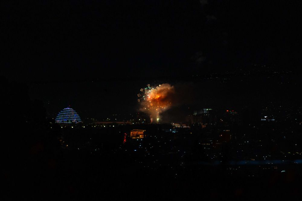 An orange and yellow plume of light ignites the dark Kigali skyline, alongside a white/blue convention centre, as part of a fireworks display to mark the start of the new year.