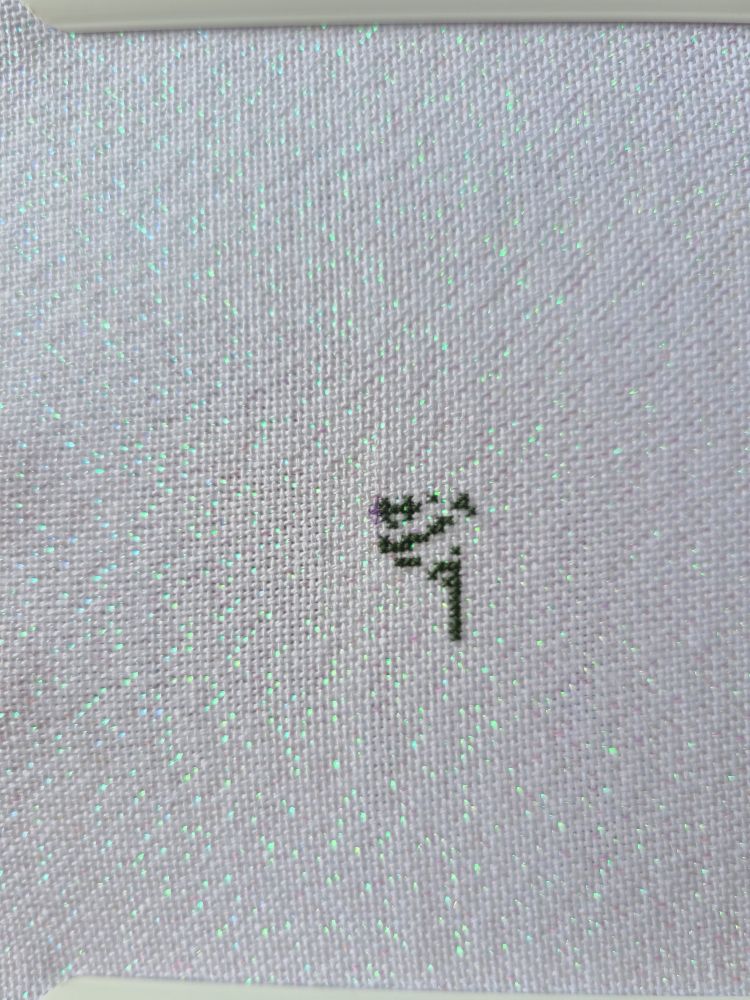 A very pale lilac sparkly cross stitch fabric with some dark green cross stitches. 