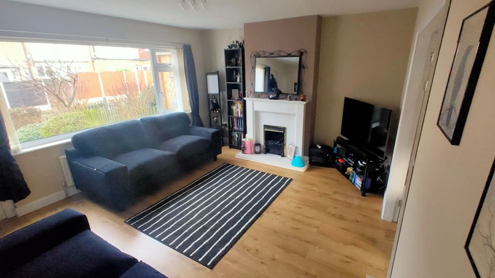 A lounge with pale walls, black sofa, black and white striped rug and a white fireplace.