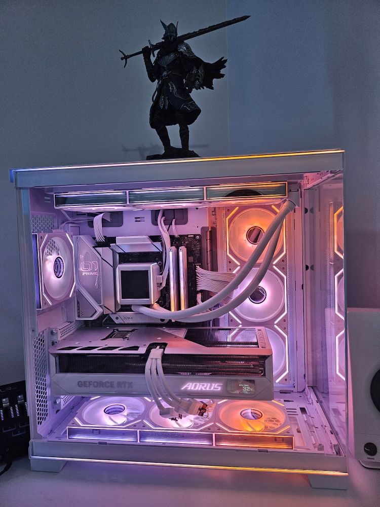 Image of a computer build. All white with the lighting in shades of purple, merging into pink and then orange.
Figurine of Wylder from the game Elden Ring Nightreign sits on top.