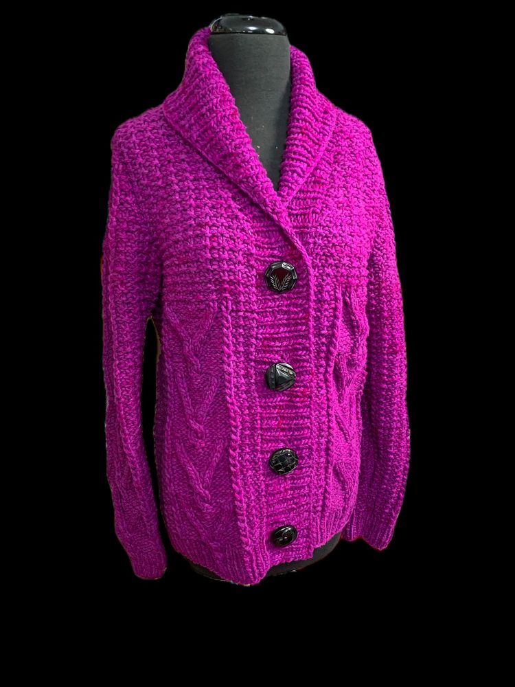 Bulky weight cardigan made from woolen spun yarn in a VERY bright shade of fuchsia/magenta. There are V shaped cables on either side, with a textured stitch pattern on the upper bodice that's maybe moss stitch (I can't remember.) There is a nice wide k2p2 button band and a fantastically deep shawl collar that sits nicely up the back of the neck. Four black vintage coat buttons close the front. Each button has a different textured surface.