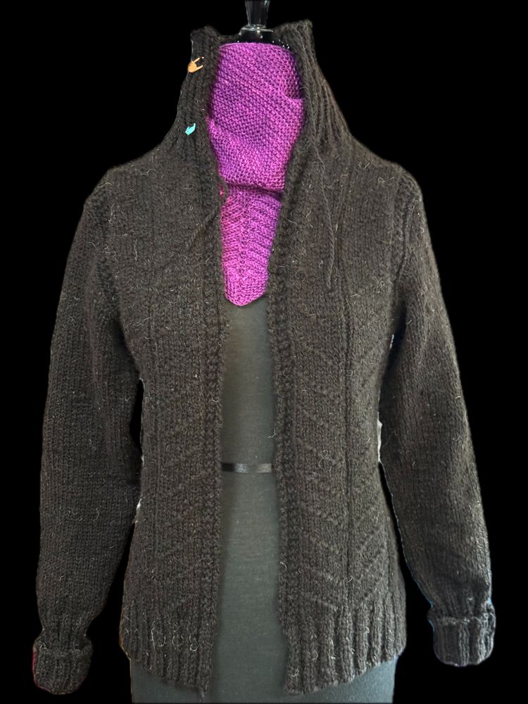 A cardigan without a front closure hangs from a mannequin. The yarn is from a black fleece (making the yarn an extremely dark, dark brown). There is a simple knit/purl texture pattern in the fabric where the purls form diagonals. Also a high ribbed neck.