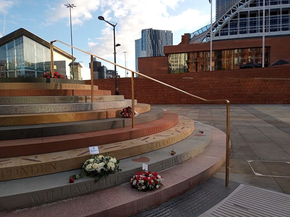 The Peterloo Memorial, with a white wreath from Manchester City council, a red and white wreath from the Peterloo Memorial Campaign, a bouquet from Manchester Histories and other flowers brought by those attending the commemoration.
