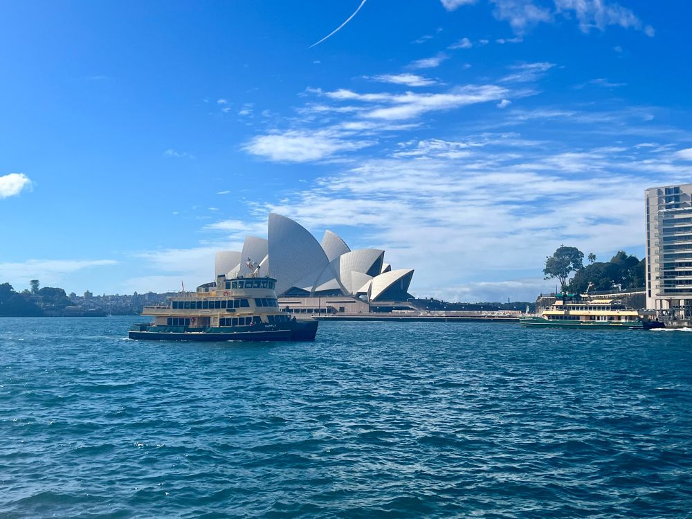 A boat driving in front of the Sydney Opera House in Sydney Harbor. 