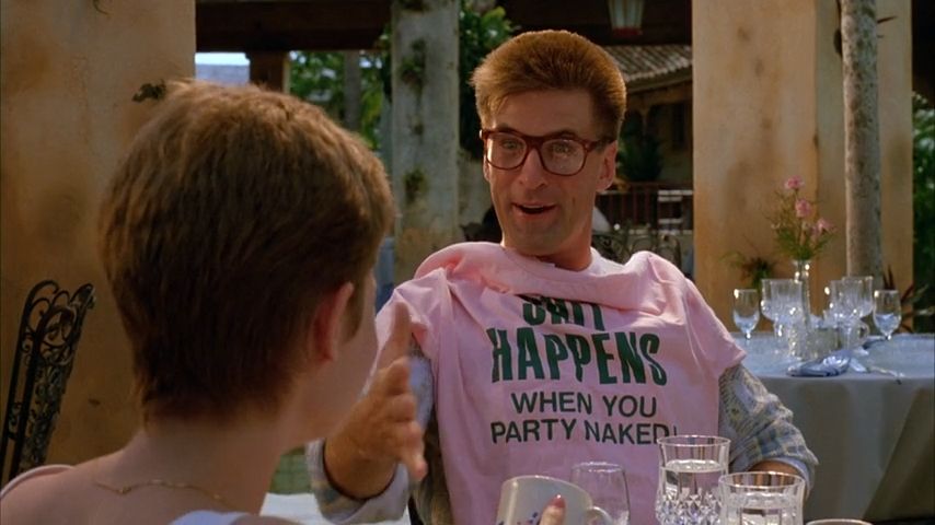 Alec Baldwin in Miami Blues (1990) wearing tortoiseshell glasses and proudly displaying a pink t-shirt reading 'SHIT HAPPENS WHEN YOU PARTY NAKED'