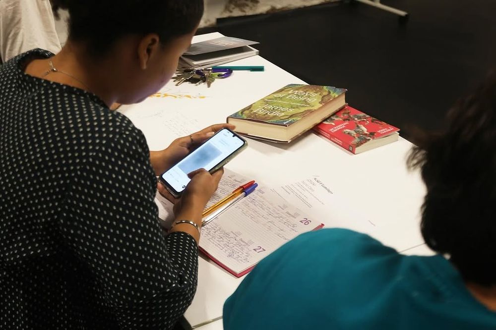 Workshop participant looking at images on her phone, she has a notebook on the table in front of her Photo: Vera Carmo