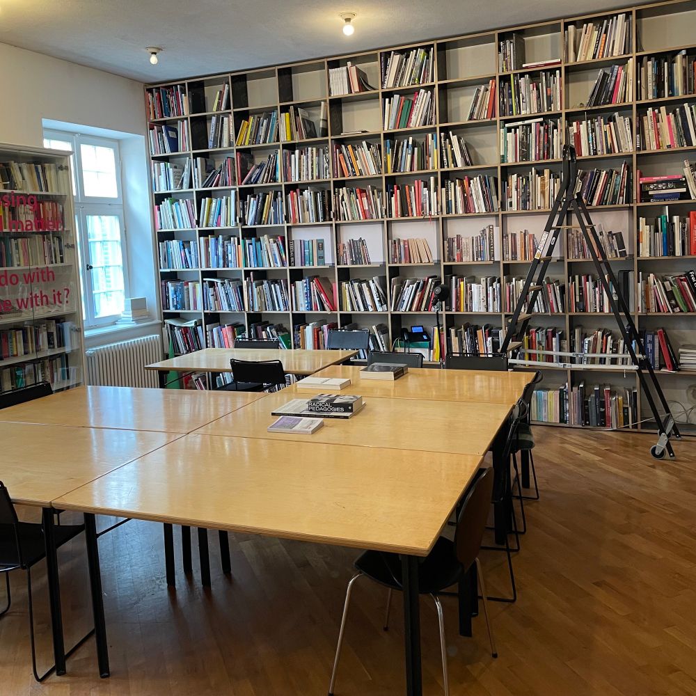 A photo of Herman’s Library at Akademie Schloss Solitude. There is a large table in the center of the room and the walls are lined with publications on art