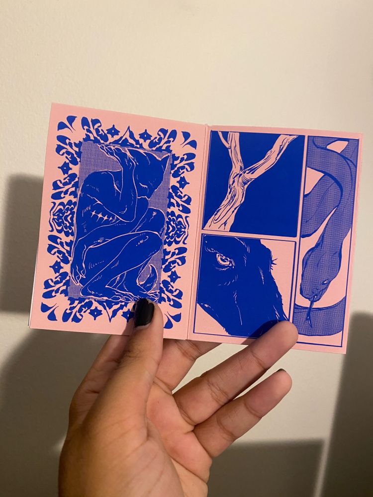 I am holding the zine open with one hand showing two pages. The left has an elaborate border with a dark figure with humanoid and dog-like features squashed within, star-ribbed scars under its chest. The page on the right has three panels, two on the left and one long vertical on the right. They read as follows: The branch of a tree white against a dark background, a closeup of the eye of a black goat, and the winding body of a snake flicking its tongue.
