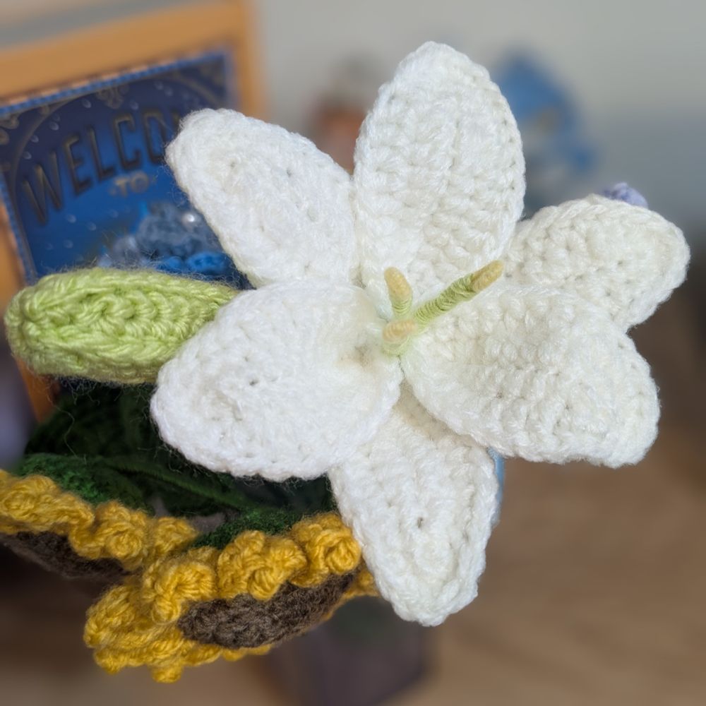 かぎ針で編んだ白い百合の花。黄緑色のつぼみがついている。下の方にはかぎ針で編んだひまわりが２輪。