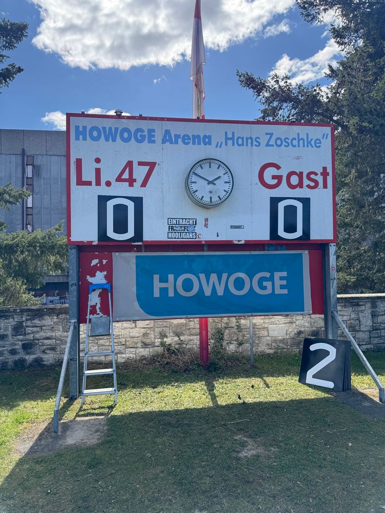 An old-school, manually updated scoreboard. It’s ten minutes til kick off, so it still says 0-0. 