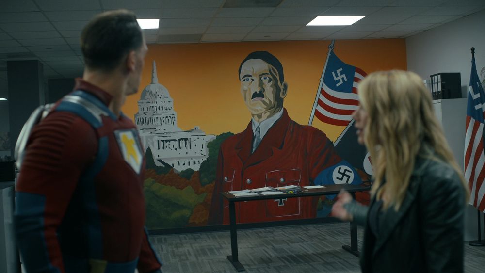 TV characters Peacemaker and Amelia Harcourt looking at a large mural of Hitler painted inside a US federal office.
