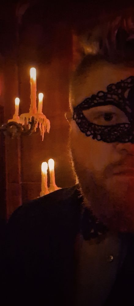 A selfie, in a masquerade mask, in front of melty candles.