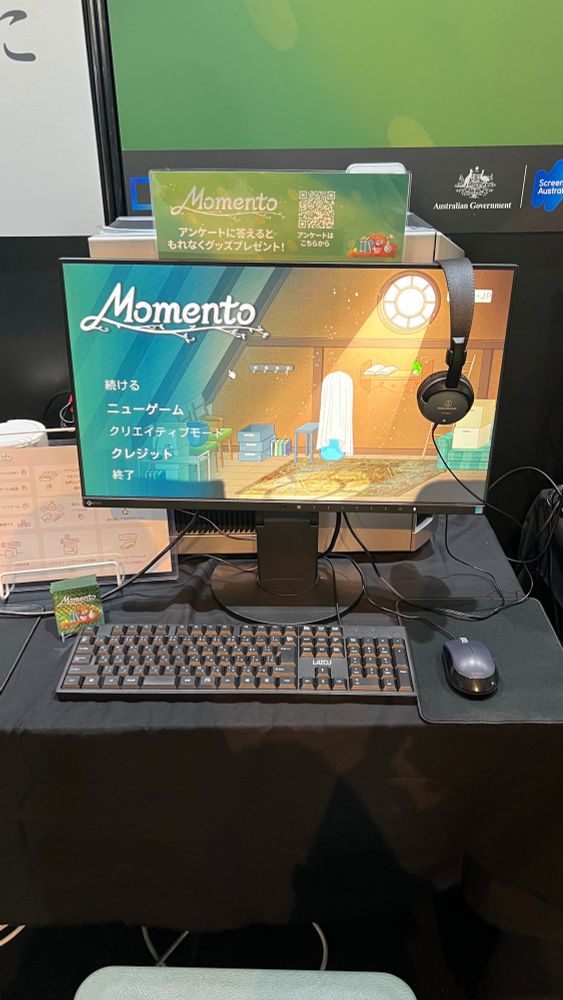 A computer monitor displays the video game Momento with the Japanese localisation active at a video game convention booth.