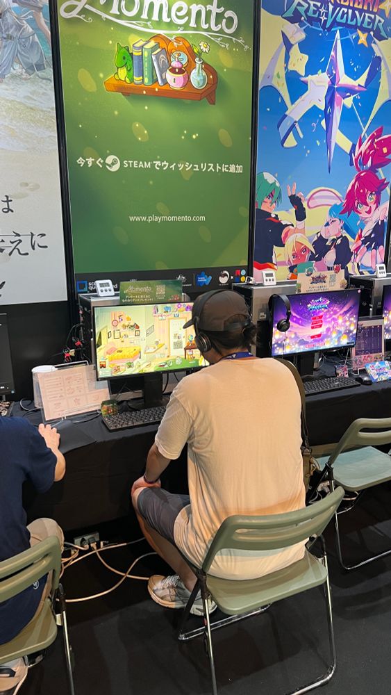A man sits at a video game convention booth, looking into a monitor displaying the video game Momento.