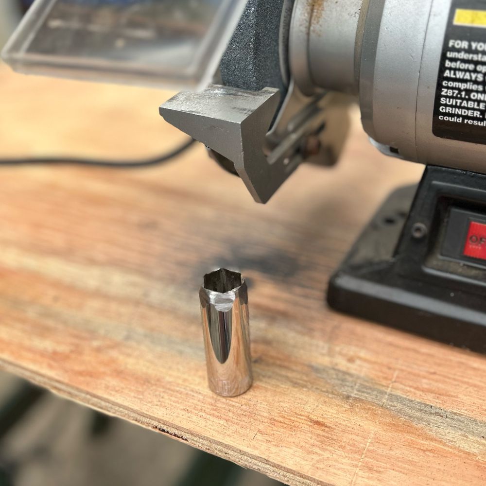 A 16mm socket sitting on a workbench in front of a bench grinder.  The tip of the socket has been ground down so the walls are thinner to fit in a tight opening.  