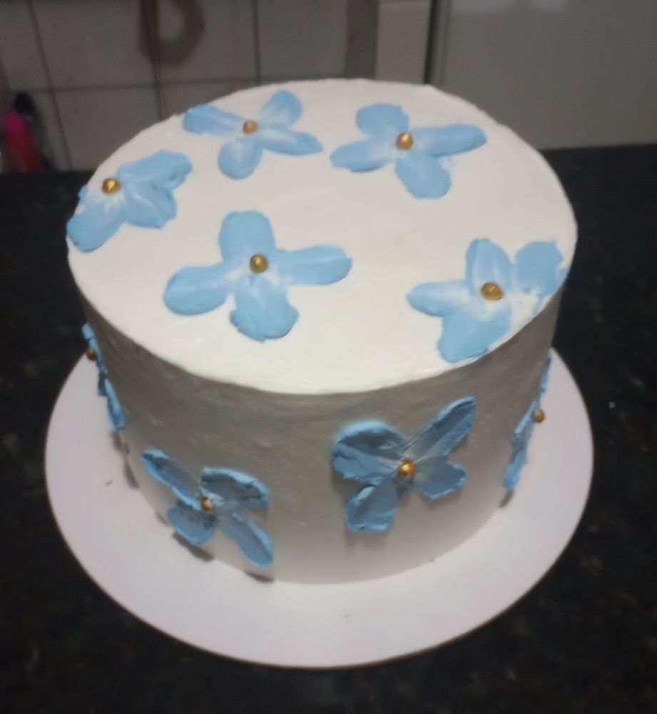 Bolo redondo com chantilly branco e enfeitado com flores azuis também de chantilly