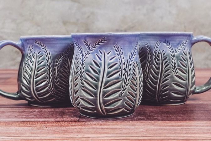 3 curvy wheel thrown mugs. Hand carved with a variety of ferns, and glazed in a blue that fades to green. 