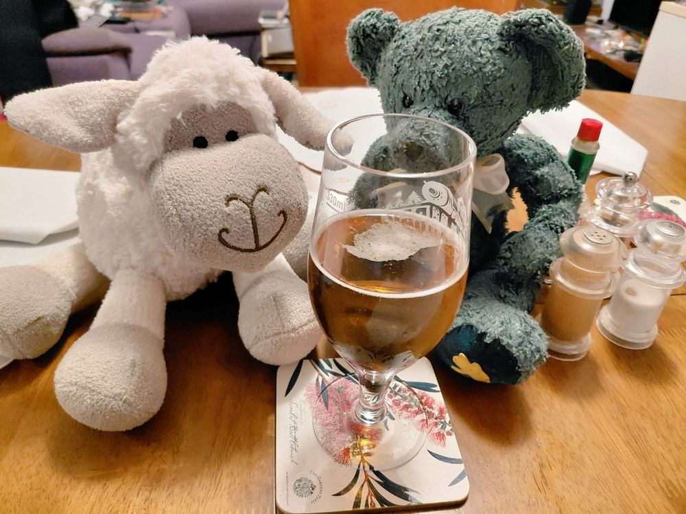 A green teddy bear and a white stuffed sheep are observing a glass of beer. 
