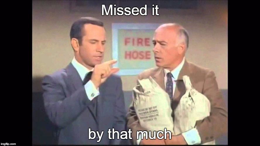 A balding man on the right holding two money bags listens to another man in a blue suit say “missed it by that much” while he is holding his hand up with his index finger and thumb about one inch apart