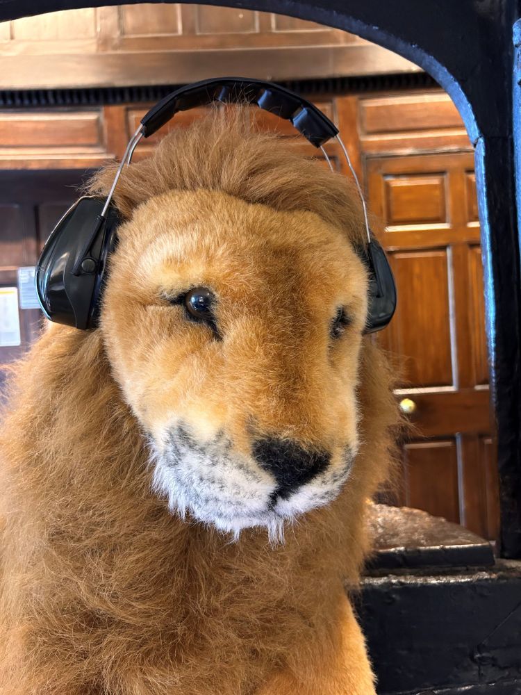 A large soft fluffy toy lion wearing a pair of black headphones.