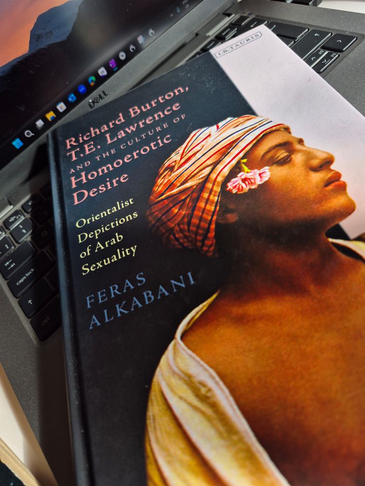 Front cover of the book Orientalist Depictions of Arab Sexuality by author and academic Feras Alkabani . The cover is dark blue and white with an image of a young man in a cloth headdress with a flower tucked into the forehead band.
