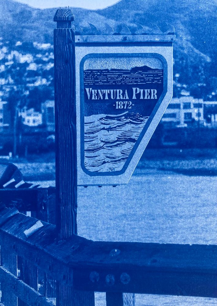 Cyanotype photo of ventura pier sign. Mountains and ocean blurry in the background