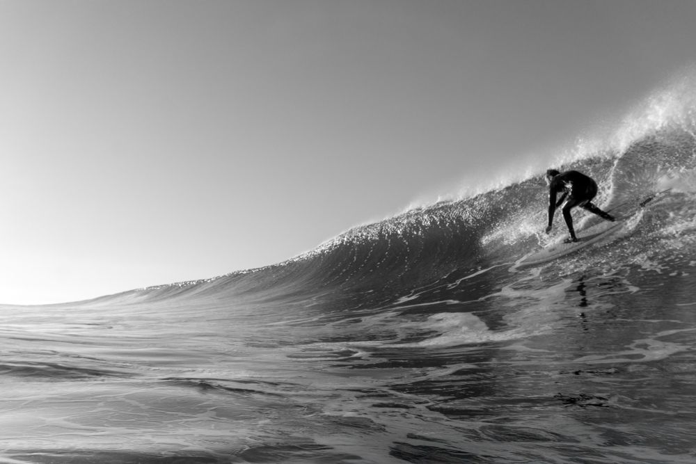 Surfer on a big wave going right. Offshore winds keeping the face open. Wave is seen off to the horizon line. 