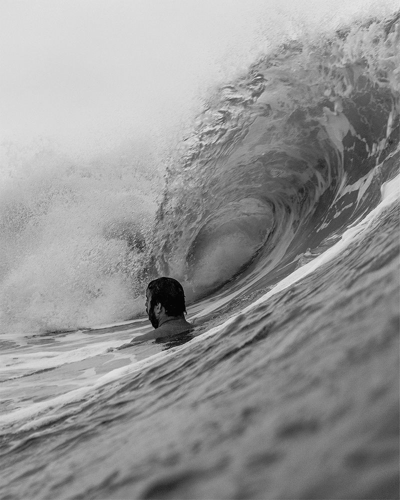 Portrait view bodysurfer looking towards the beach as a barreling wave is about to pass overhead