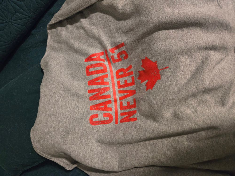 A grey hoodie with the words "Canada Never 51" and a maple leaf in red on the back