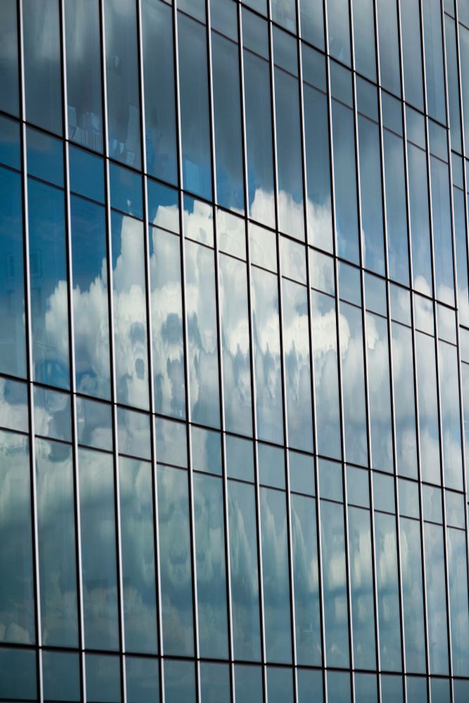 A reflection of a cloud off of the side of a glass building.