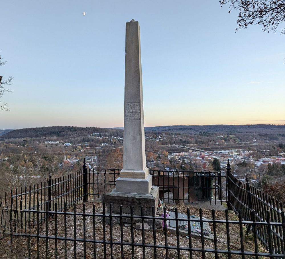 Cemetery monument surrounded by black wrought iron fence on hilltop at dusk