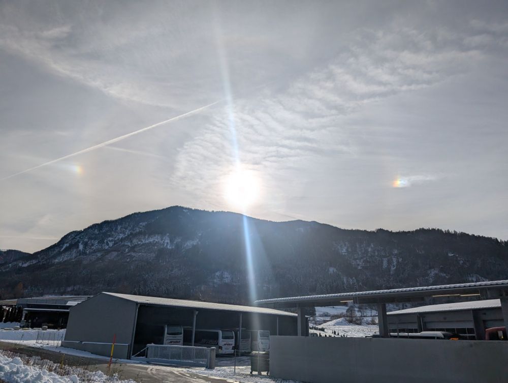 the picture shows a mountain, the sun and two bright sundogs